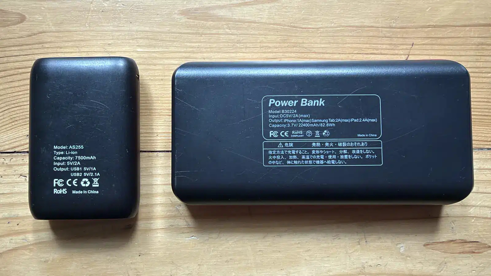 Zwei Powerbanks mit 7500 mAh und 22400 mAh nebeneinander auf Holz, Kapazitätsangabe auf dem Gehäuse