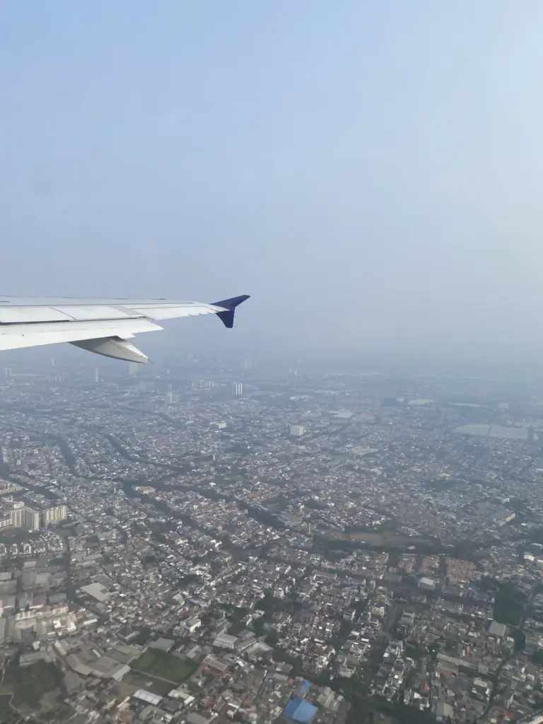 Flugzeugflügel im Landeanflug über einer Großstadt im Dunst