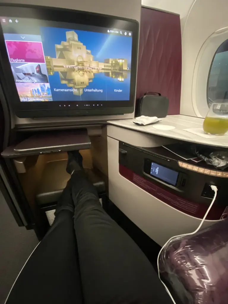 Beinfreiheit in der Qatar Airways QSuite mit ausgestreckten Beinen und Fußraum unter dem Bildschirm