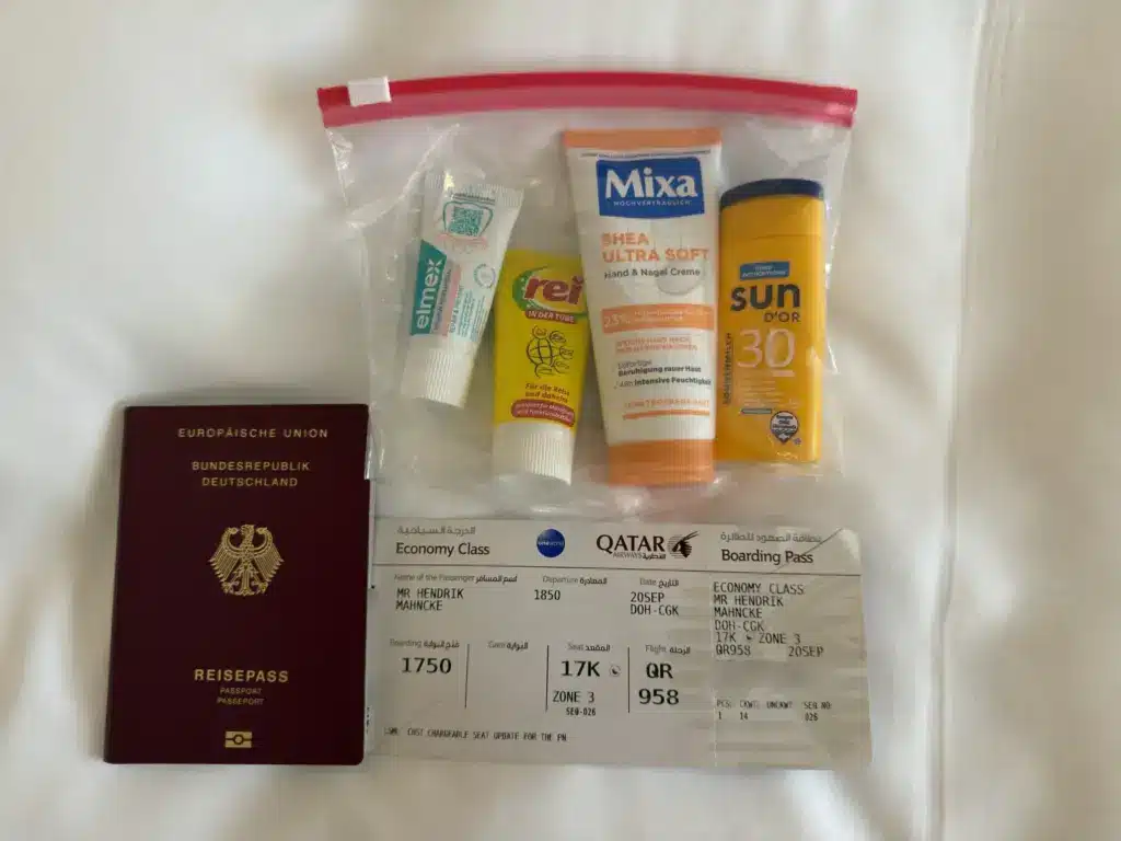 Durchsichtiger Beutel mit Zahnpasta, Reisewaschmittel, Handcreme und Sonnenmilch neben Reisepass und Bordkarte