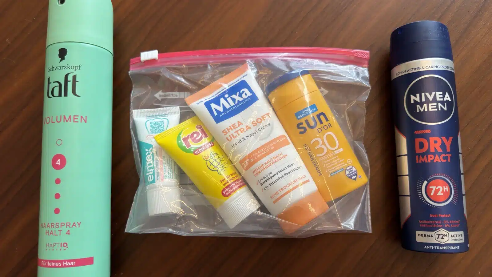 Haarspray, Beutel mit Reisegrößen und Spraydeo nebeneinander auf einem Holztisch