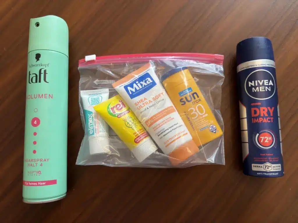 Durchsichtiger Beutel mit Zahnpasta, Reisewaschmittel, Handcreme und Sonnenmilch zwischen Taft Haarspray und Nivea Deo