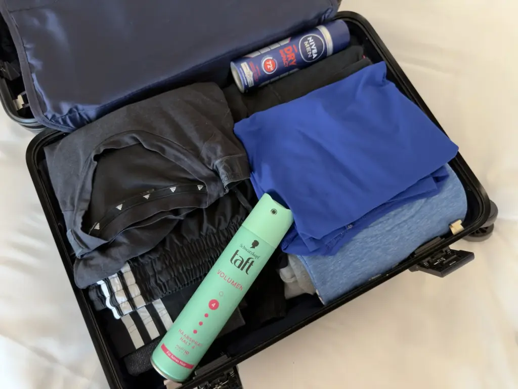 Offener Koffer mit Kleidung, darauf ein Taft Haarspray und ein Nivea Men Deo