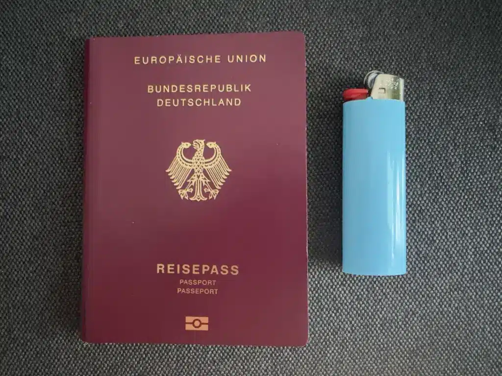 Deutscher Reisepass neben einem hellblauen Einwegfeuerzeug auf dunklem Stoff