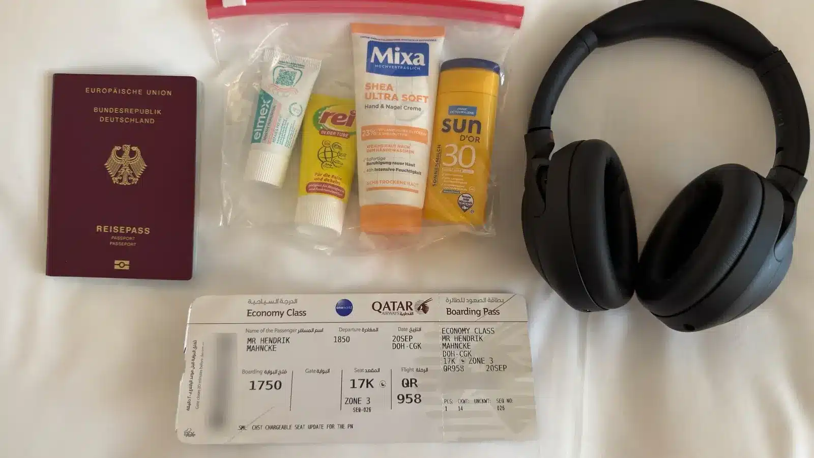 Reisepass, Beutel mit Reisegrößen, Kopfhörer und Bordkarte nebeneinander auf einem weißen Laken