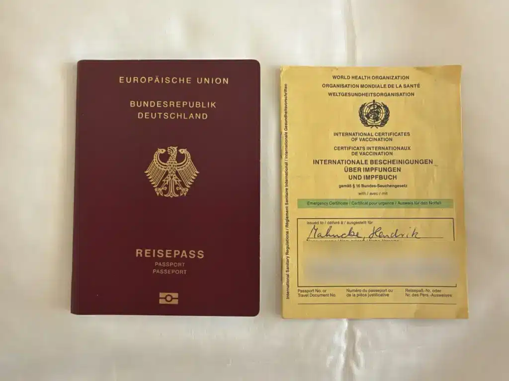 Deutscher Reisepass und internationaler Impfausweis nebeneinander auf einem weißen Laken
